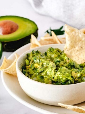 Guacamole with chips on white table.
