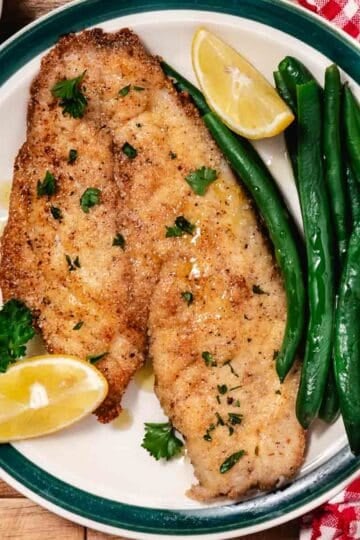 Fried yellowtail snapper with green beans and lemon slices.