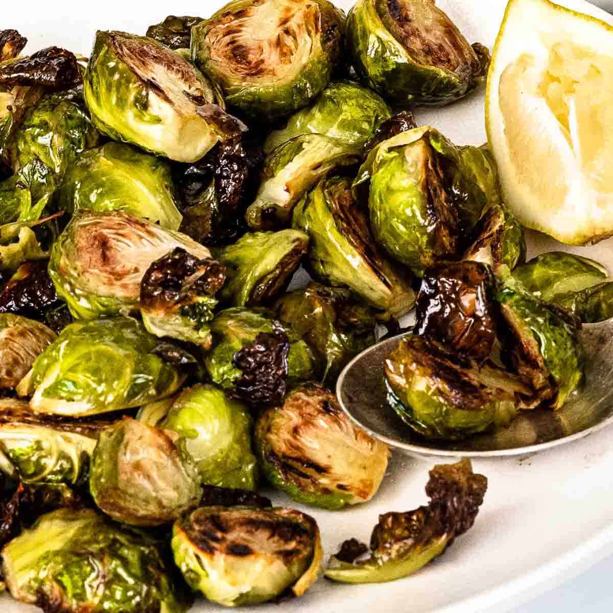 Roasted Brussels sprouts on a white plate with q lemon wedge.