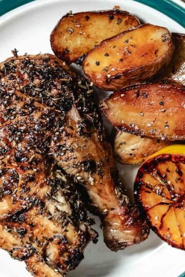 Roasted chicken leg quarter with crispy potatoes and charred lemon on a plate