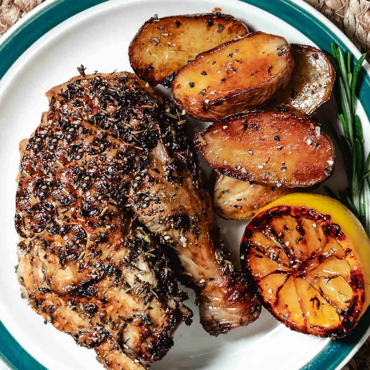 Quarter roasted chicken with golden brown exterior served with potatoes and lemons.