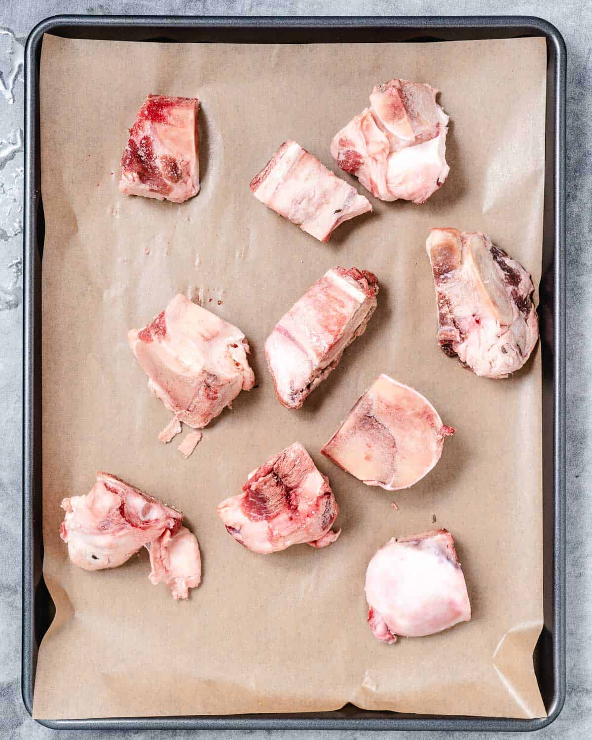 Beef bones on parchment lined baking sheet.