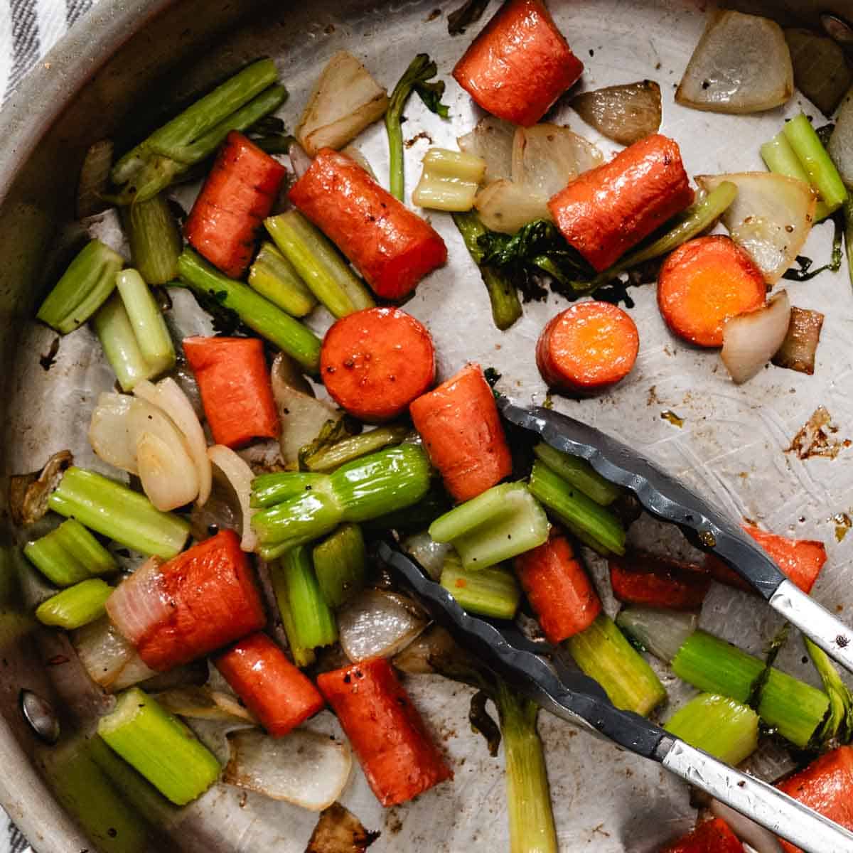 Sautéed carrots, celery, and onions browning in a skillet to build flavor before adding to bone broth.