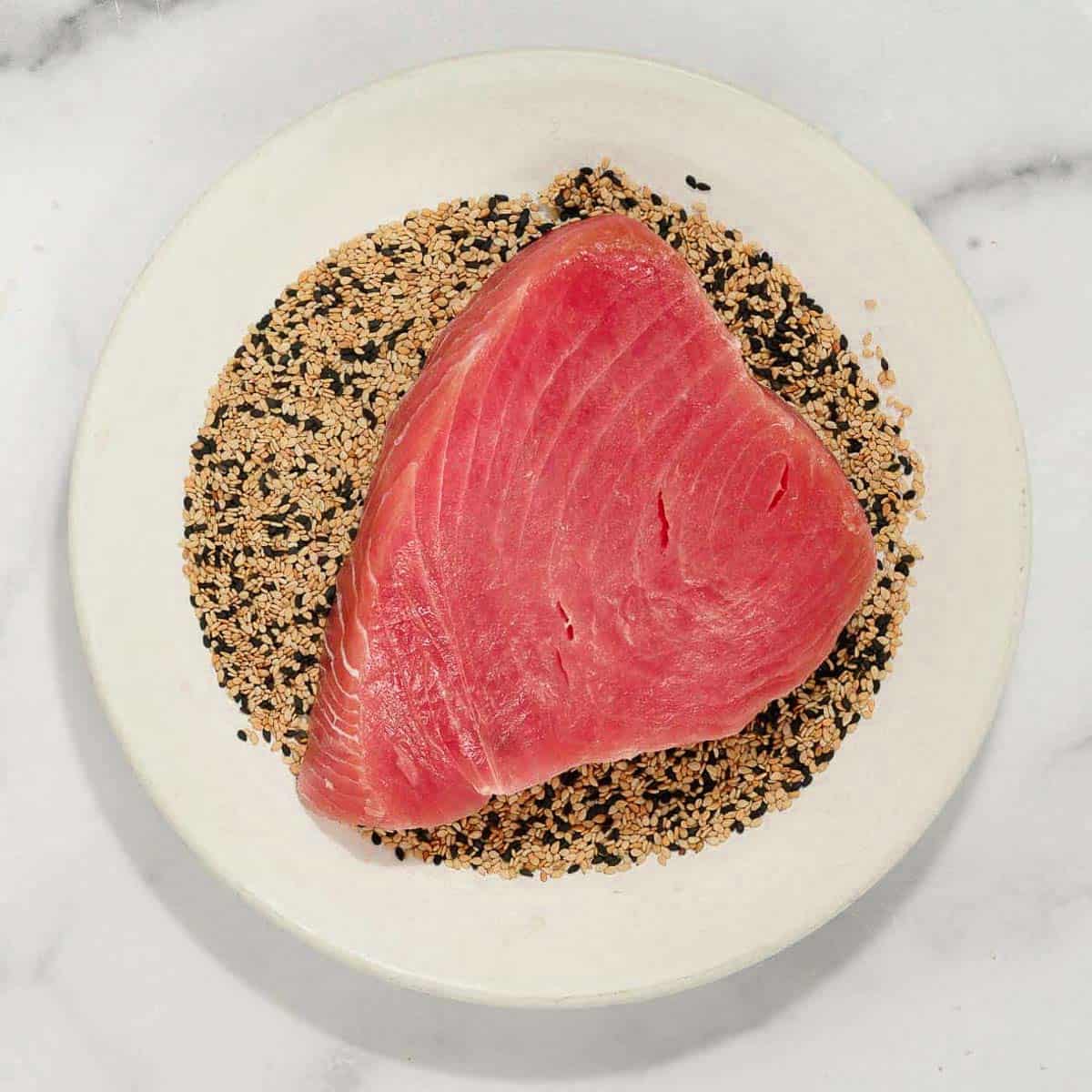 Raw ahi tuna on plate of sesame seeds.