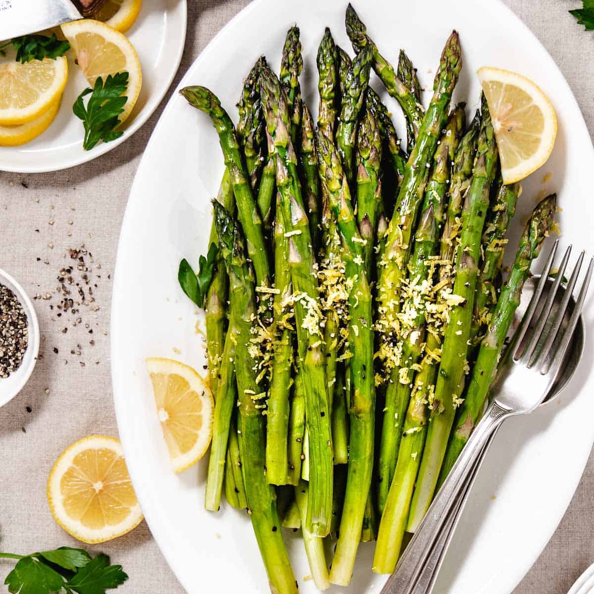 roasted asparagus with lemon zest on a white tray with lemon slices.
