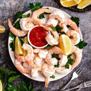 Shrimp cocktail in a bowl with cocktail sauce and lemons.