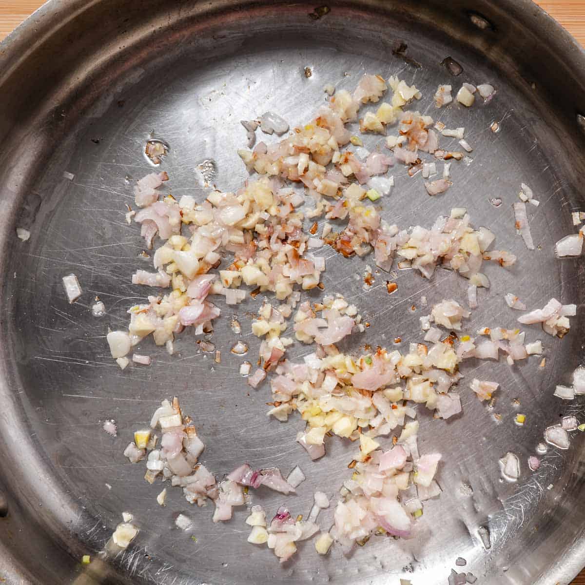 Chopped shallots and garlic cooking in olive oil in a stainless-steel sauté pan.
