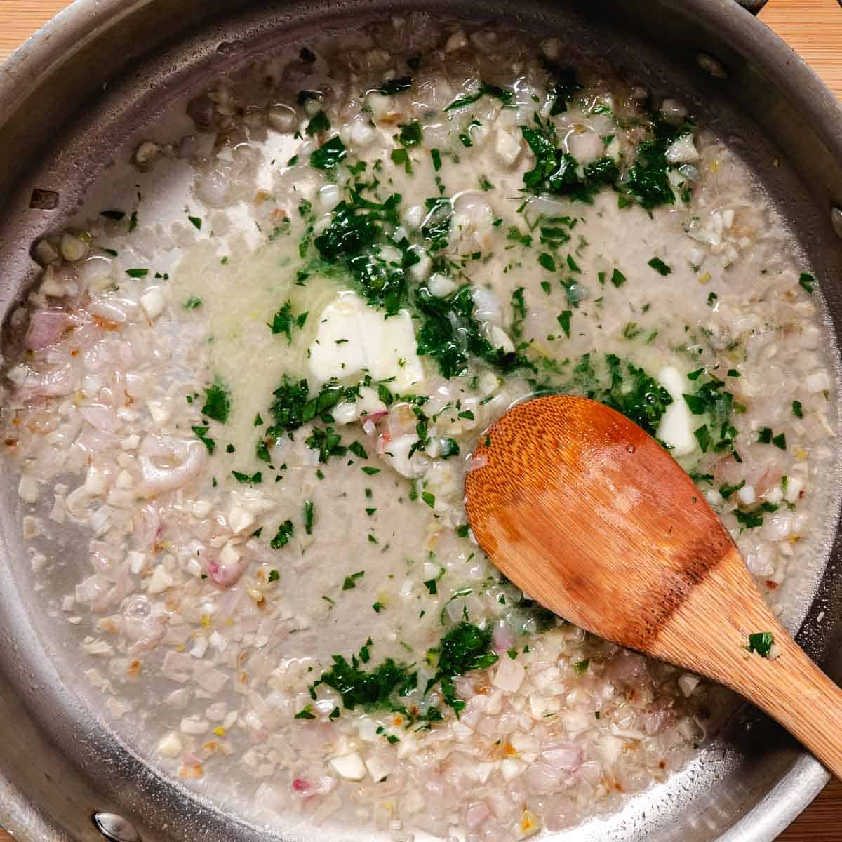 Shallots, garlic, butter, white wine, and parsley simmering in a stainless-steel sauté pan.