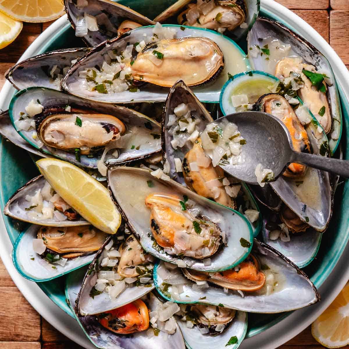 Green-lipped mussels on the half shell served with garlic butter wine sauce and lemon wedges.