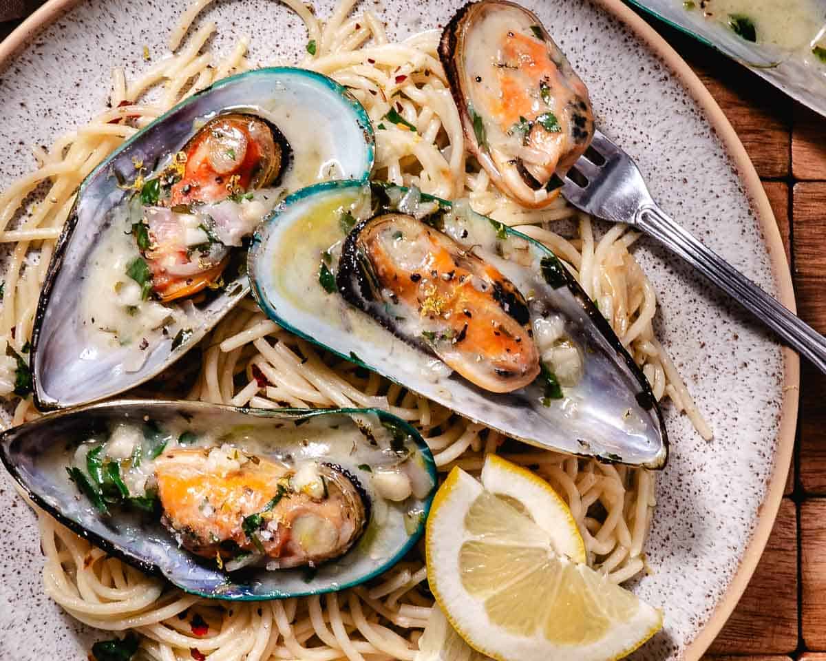 New Zealand green-lipped mussels served over spaghetti with garlic butter white wine sauce and a lemon wedge.