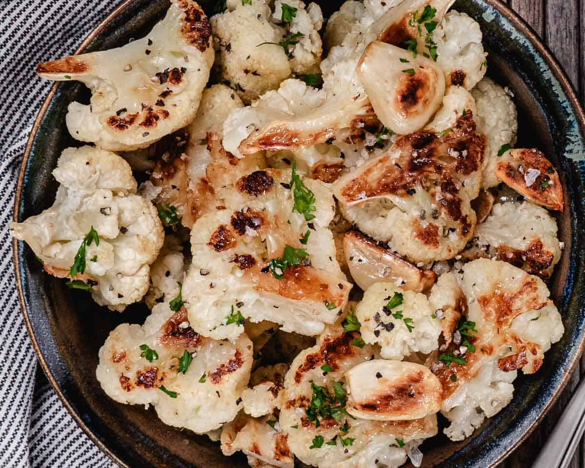 Roasted cauliflower with whole caramelized garlic cloves, chopped parsley, salt, and black pepper.