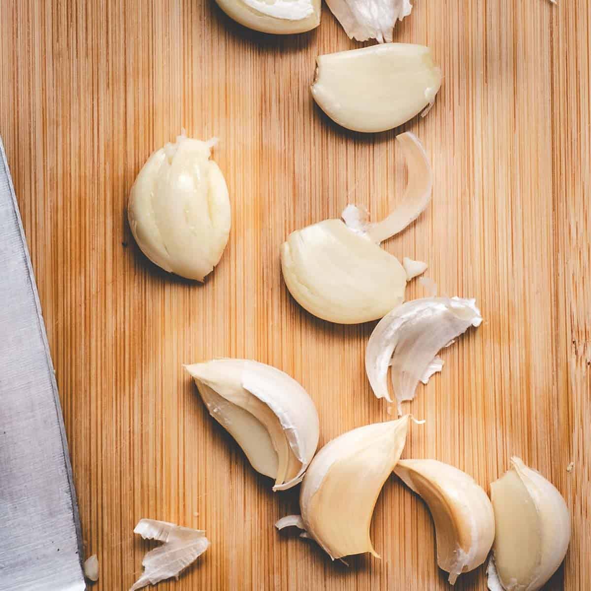 Peeled garlic cloves on a board with a knife.