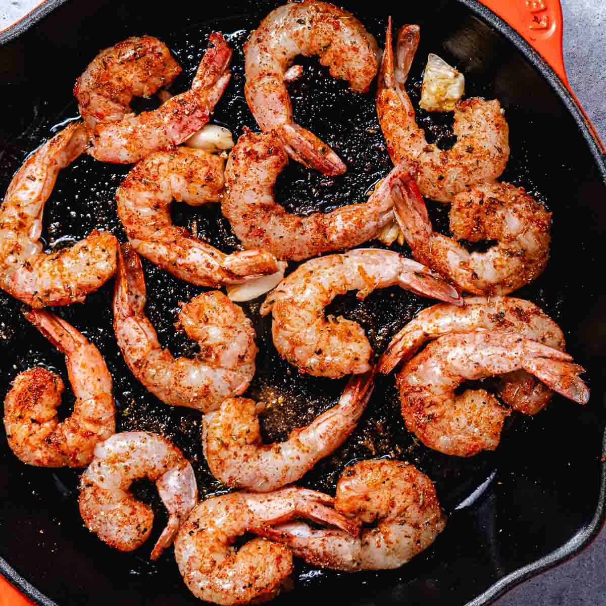 Blackened shrimp cooking in a hot cast iron skillet with garlic and oil.