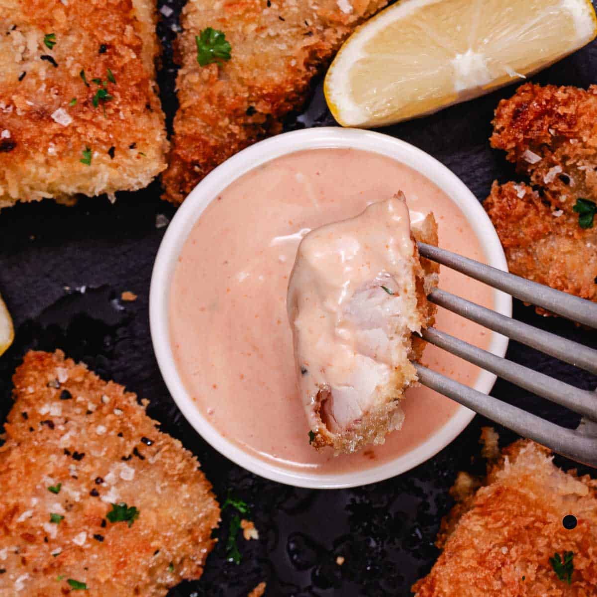 A forkful of crispy red snapper dipped in sauce, showing the flaky white interior under the panko crust