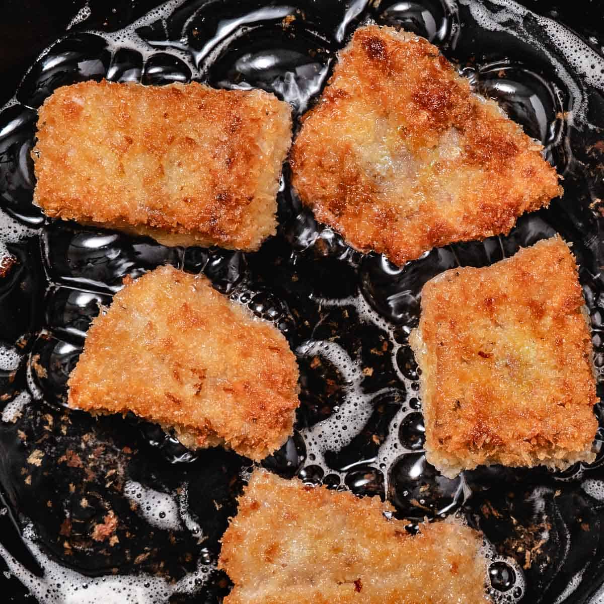 Five panko-crusted red snapper fillets frying in hot oil, turning golden brown and crispy