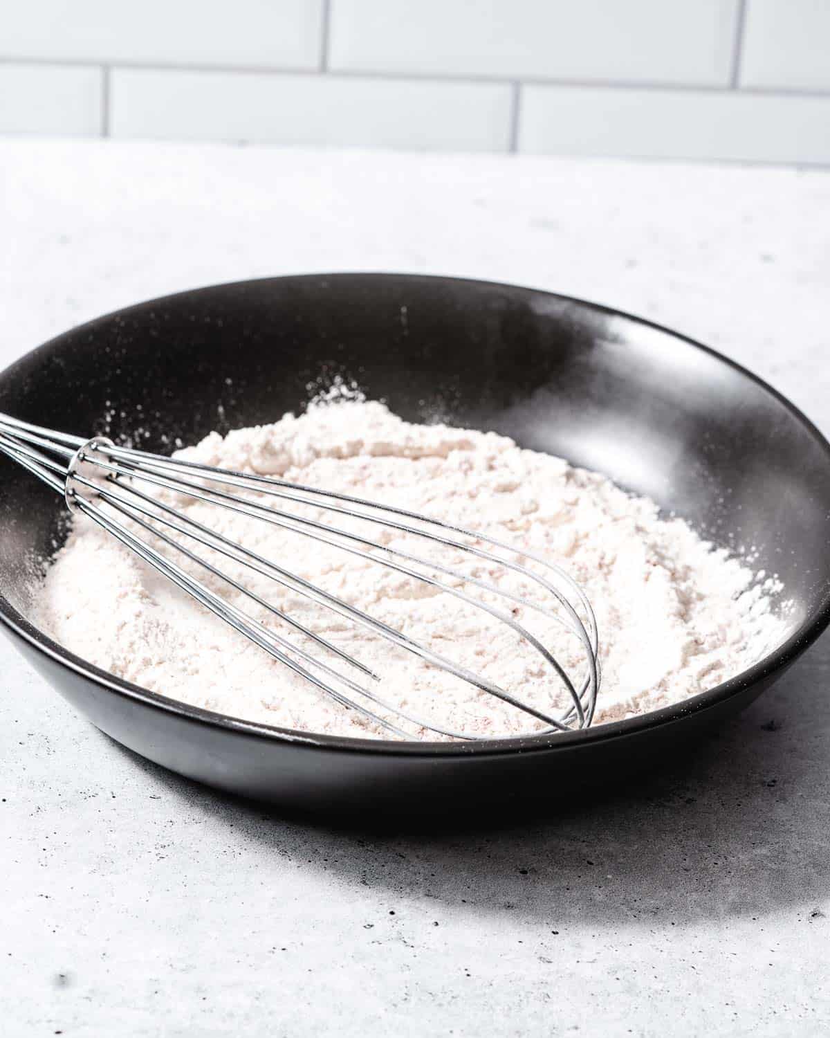 A bowl of flour with a whisk.