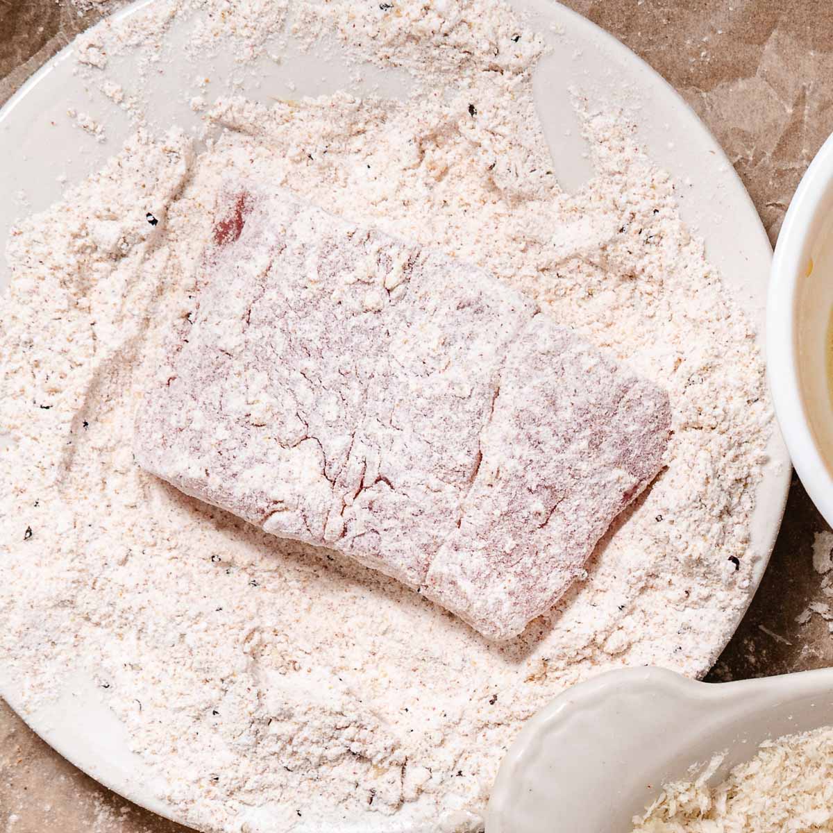 Red snapper fillet dredged in seasoned flour on a plate, first step of breading before the egg dip
