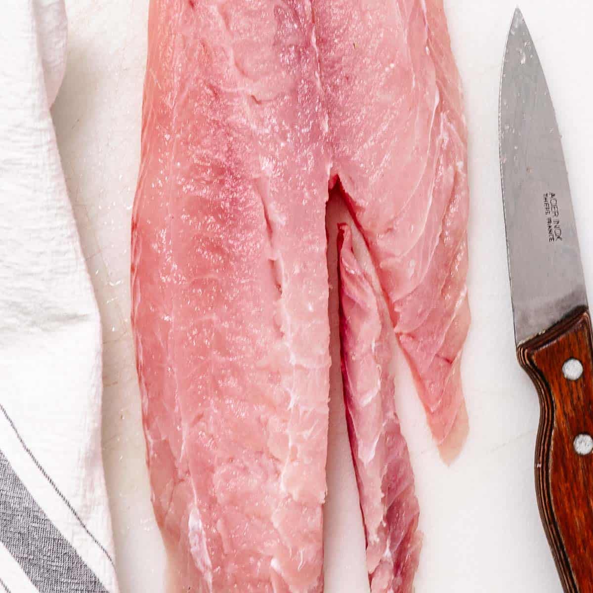 Fresh red snapper fillet on a cutting board being trimmed with a knife before breading