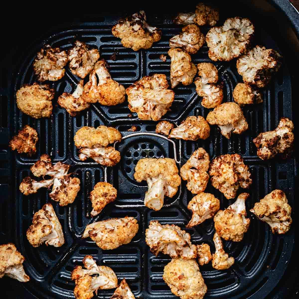 Golden brown roasted cauliflower in an air fryer basket