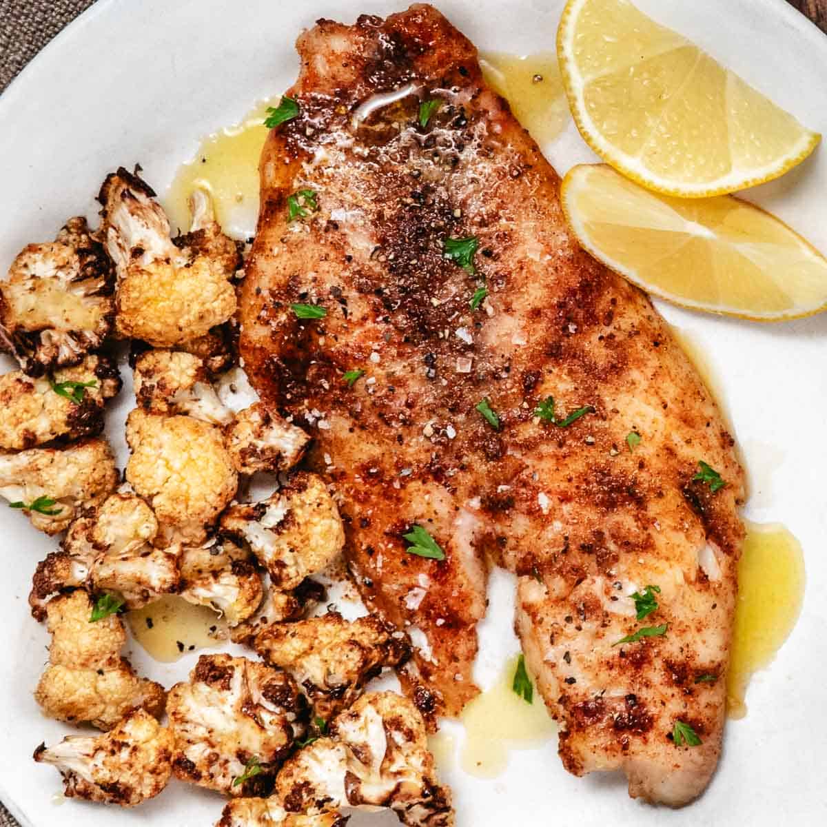Plate of air fryer snapper with cooked cauliflower and lemon wedges.