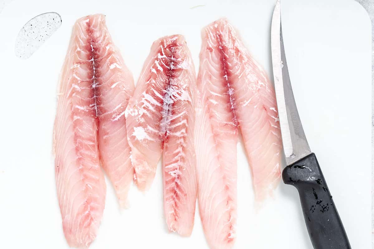 Snapper fillets with knife on white.