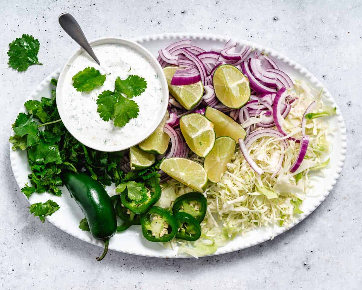 Toppings for fish tacos: cabbage, onions, limes, jalapenos, cilantro, sour cream dressing.