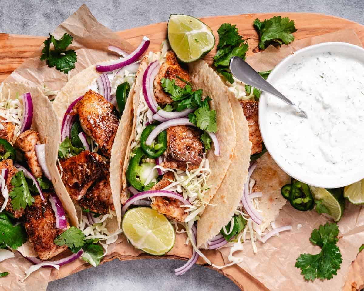 Coked snapper tacos with cilantro lime cream and cabbage on a board.
