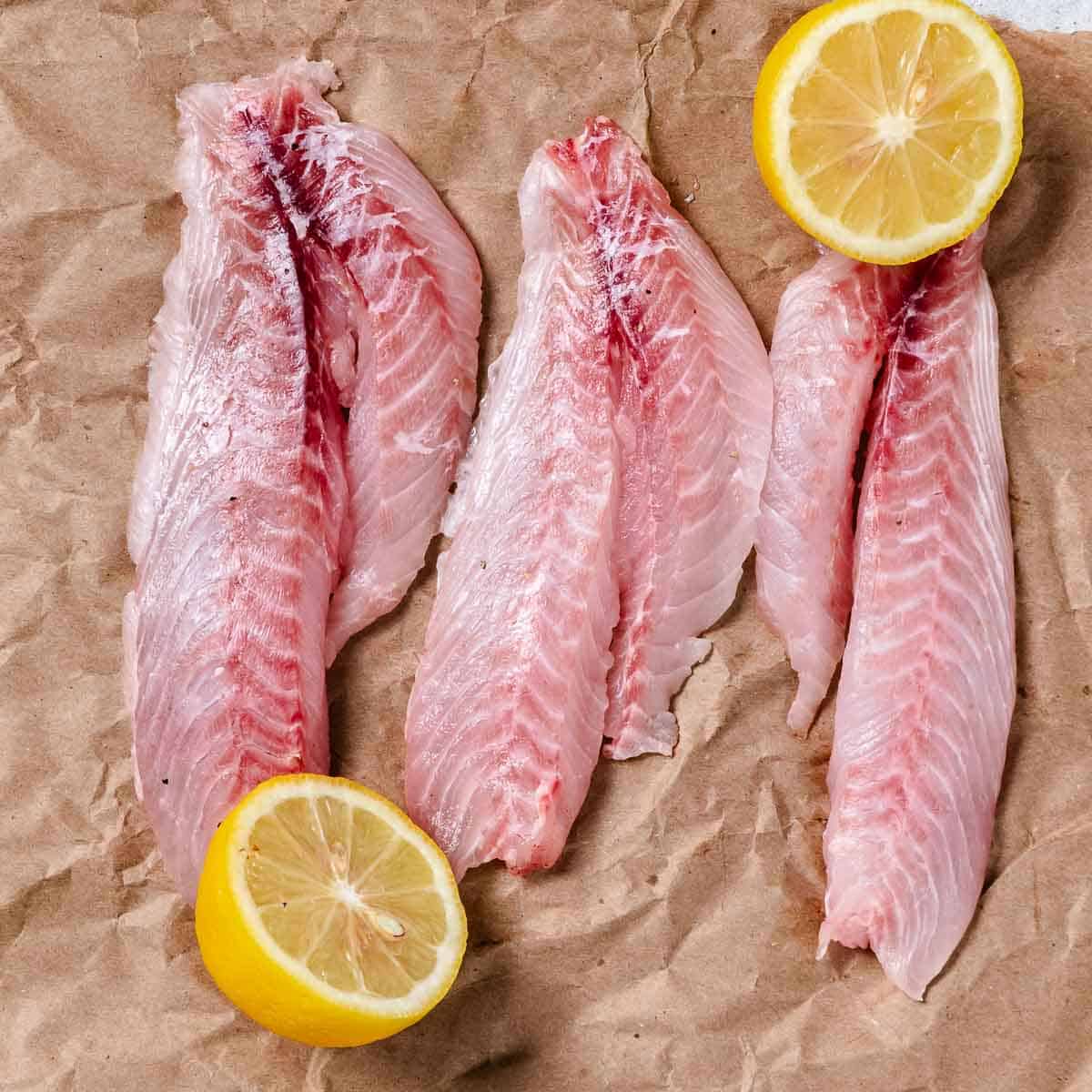 Fresh yellowtail snapper fillets with lemon halves.