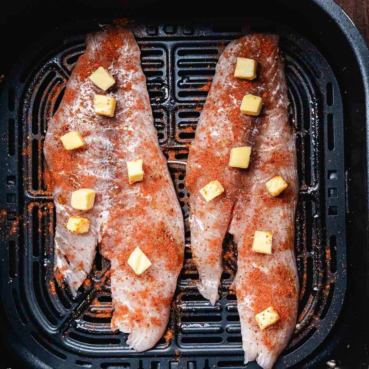 Snapper fillets seasoned with Old Bay and butter in an air fryer basket