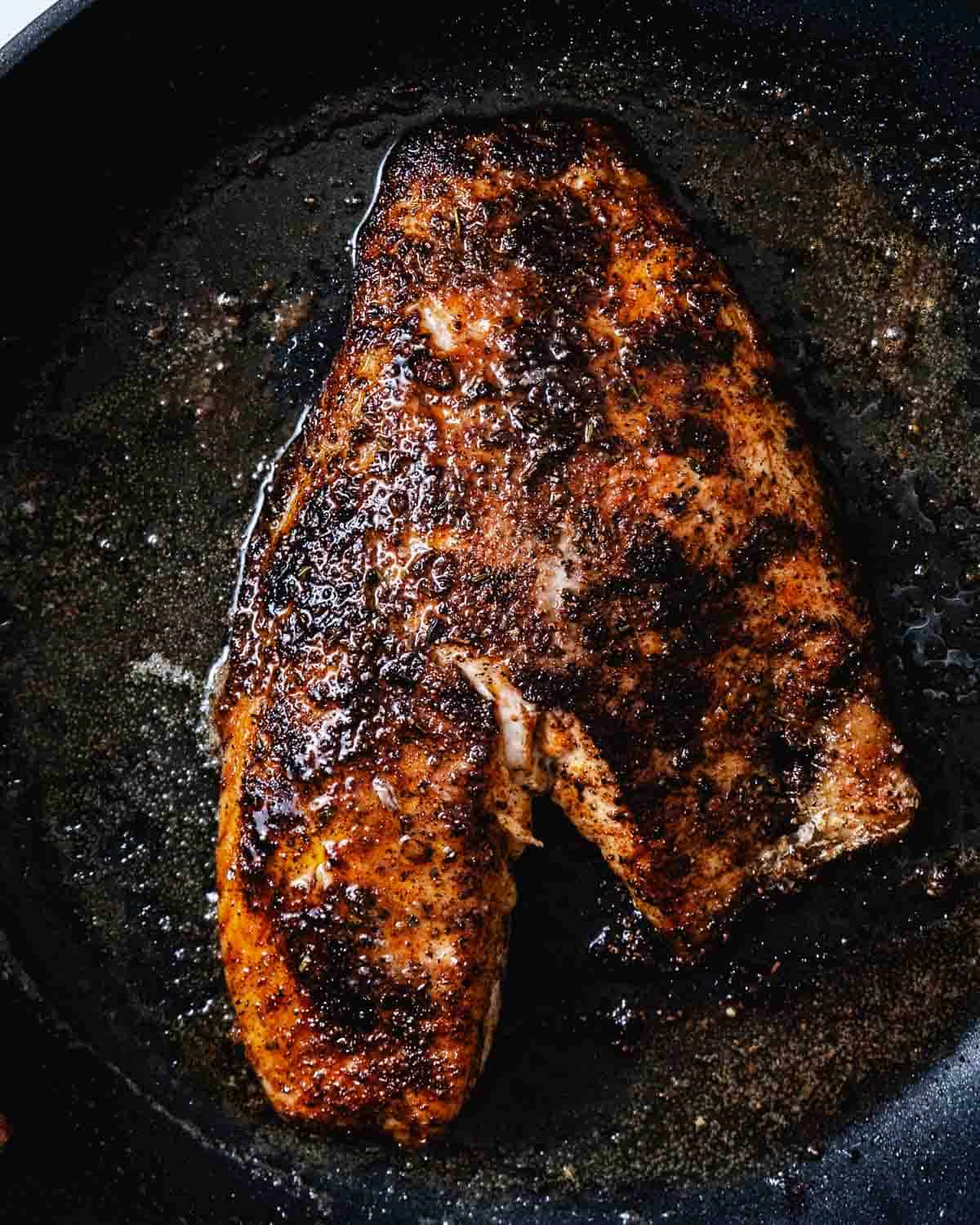 Blackened snapper cooking in a cast-iron skillet