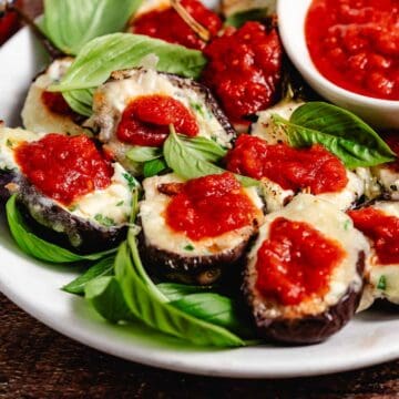Baby eggplant parmigiana with basil leaves on white plate.