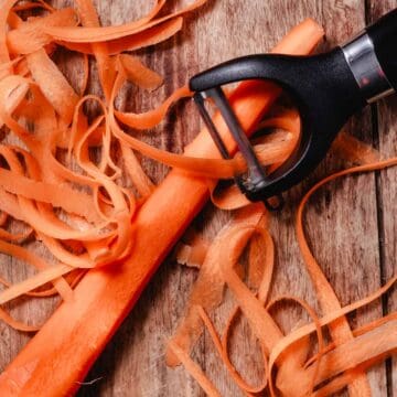 vegetable peeler shaving fresh carrot ribbons on a rustic wood surface for carrot salad