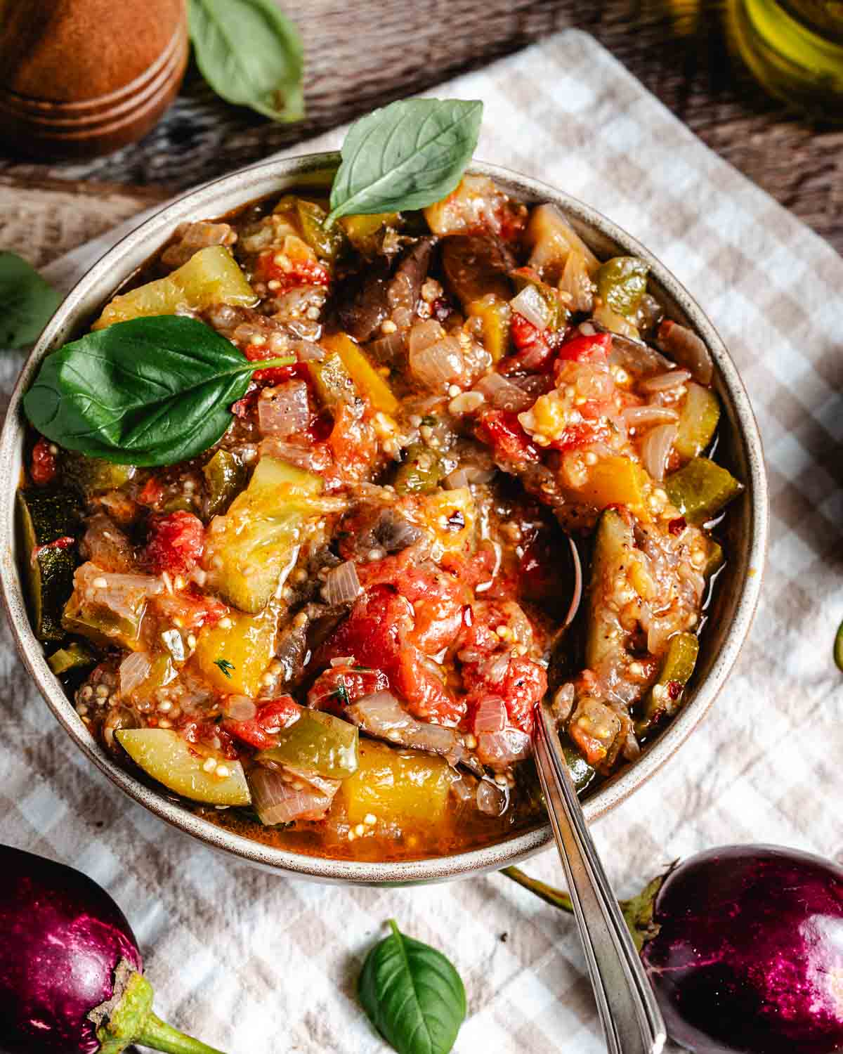 A bowl of traditional French ratatouille on gingham napkin with baby eggplants.