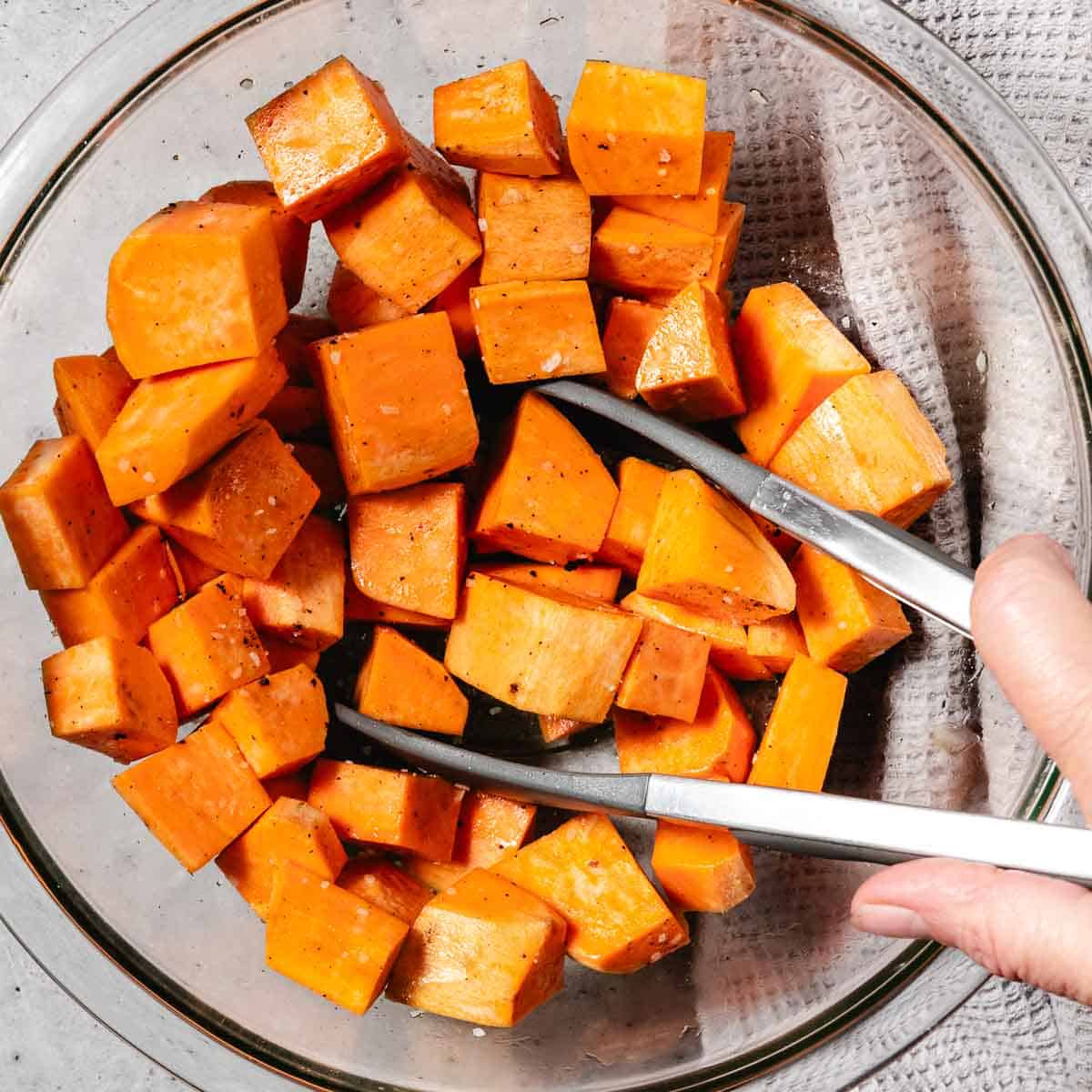 mixing baked sweet potato cubes with oil and seasonings