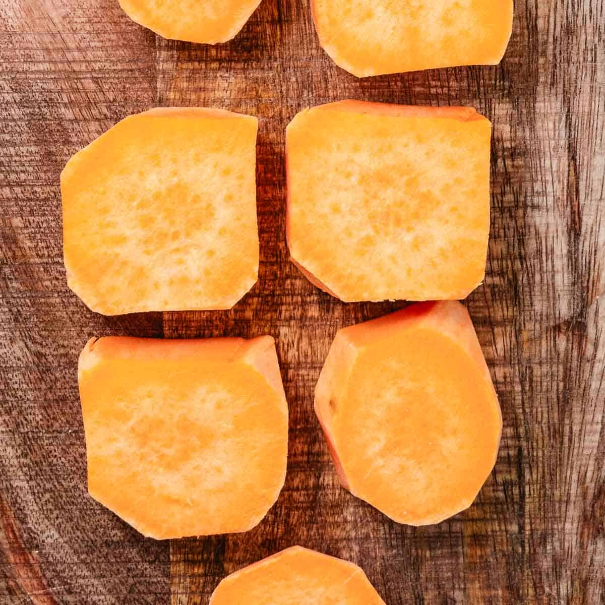 Peeled sweet potato cut crosswise into 1-inch rounds on a wooden cutting board.