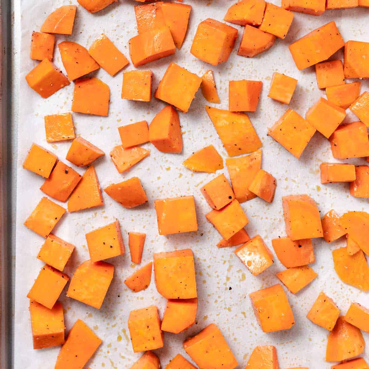 Cubed sweet potatoes seasoned with olive oil, salt, and pepper on a parchment-lined baking sheet.