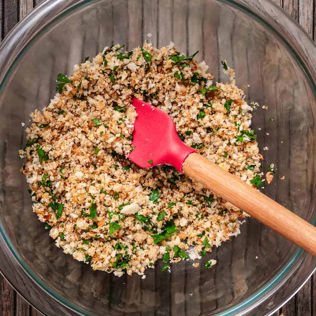 Breadcrumb, Parmesan, butter, and parsley topping mixed in a glass bowl with a spatula.