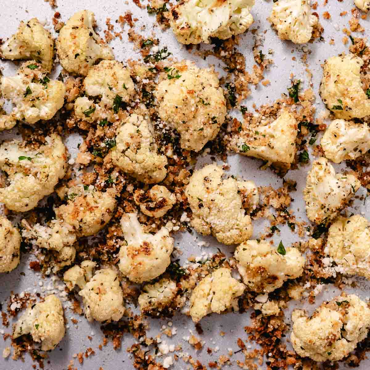 Roasted cauliflower florets with golden breadcrumbs, Parmesan cheese, and chopped parsley on a sheet pan.