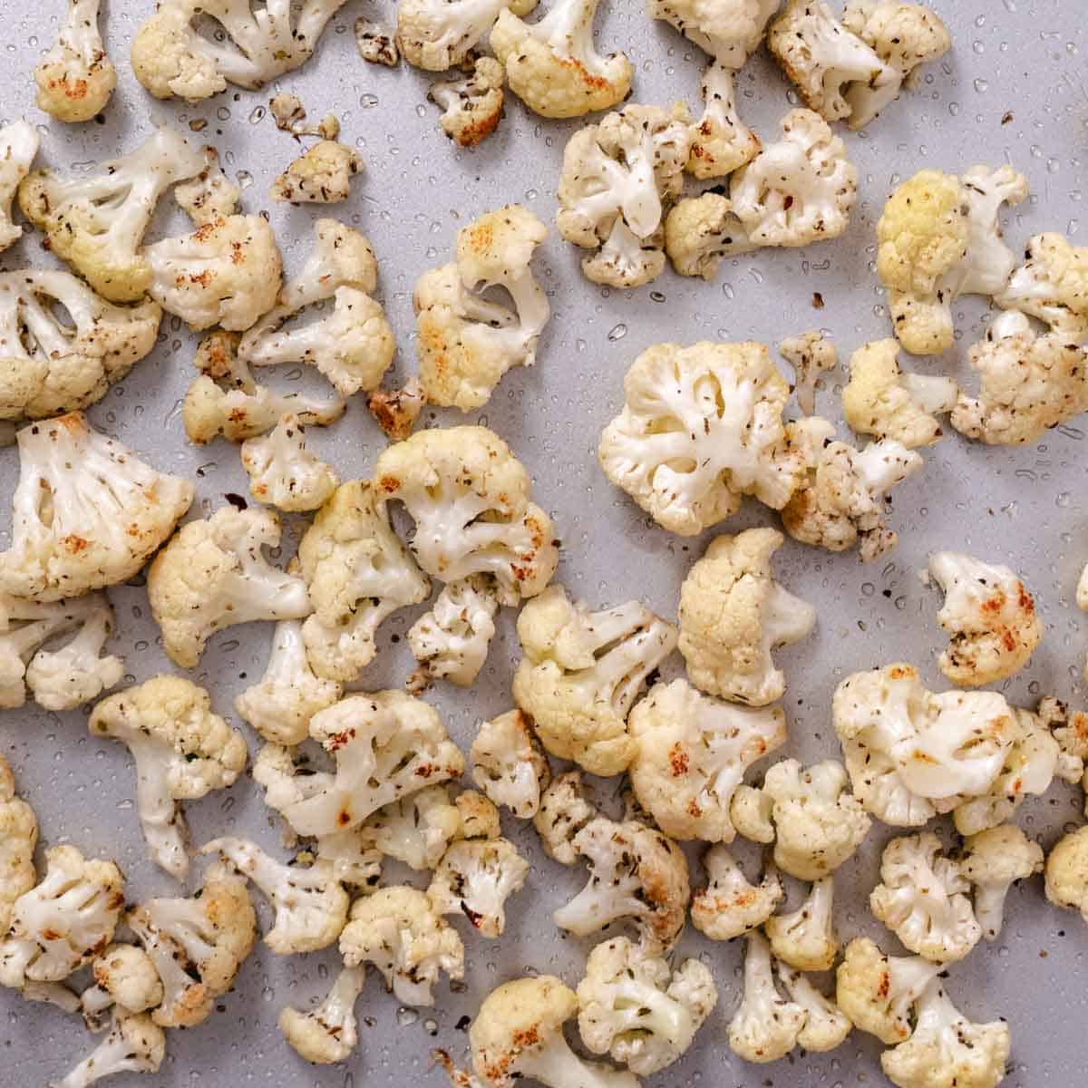 Seasoned cauliflower florets beginning to brown on a sheet pan after roasting.