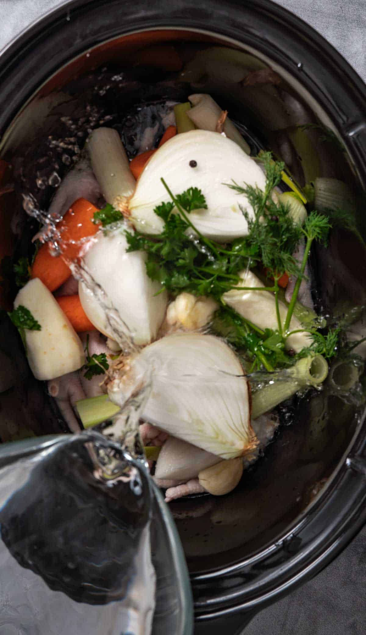 Filling a crock pot with liquid over chicken parts and veggies.