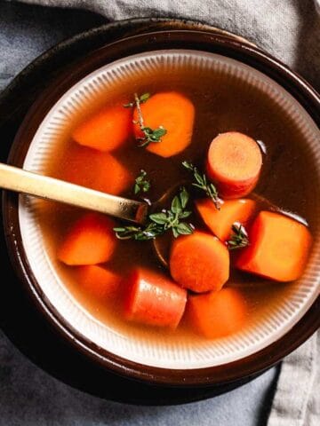 Bowl of chicken soup with carrots and thyme.