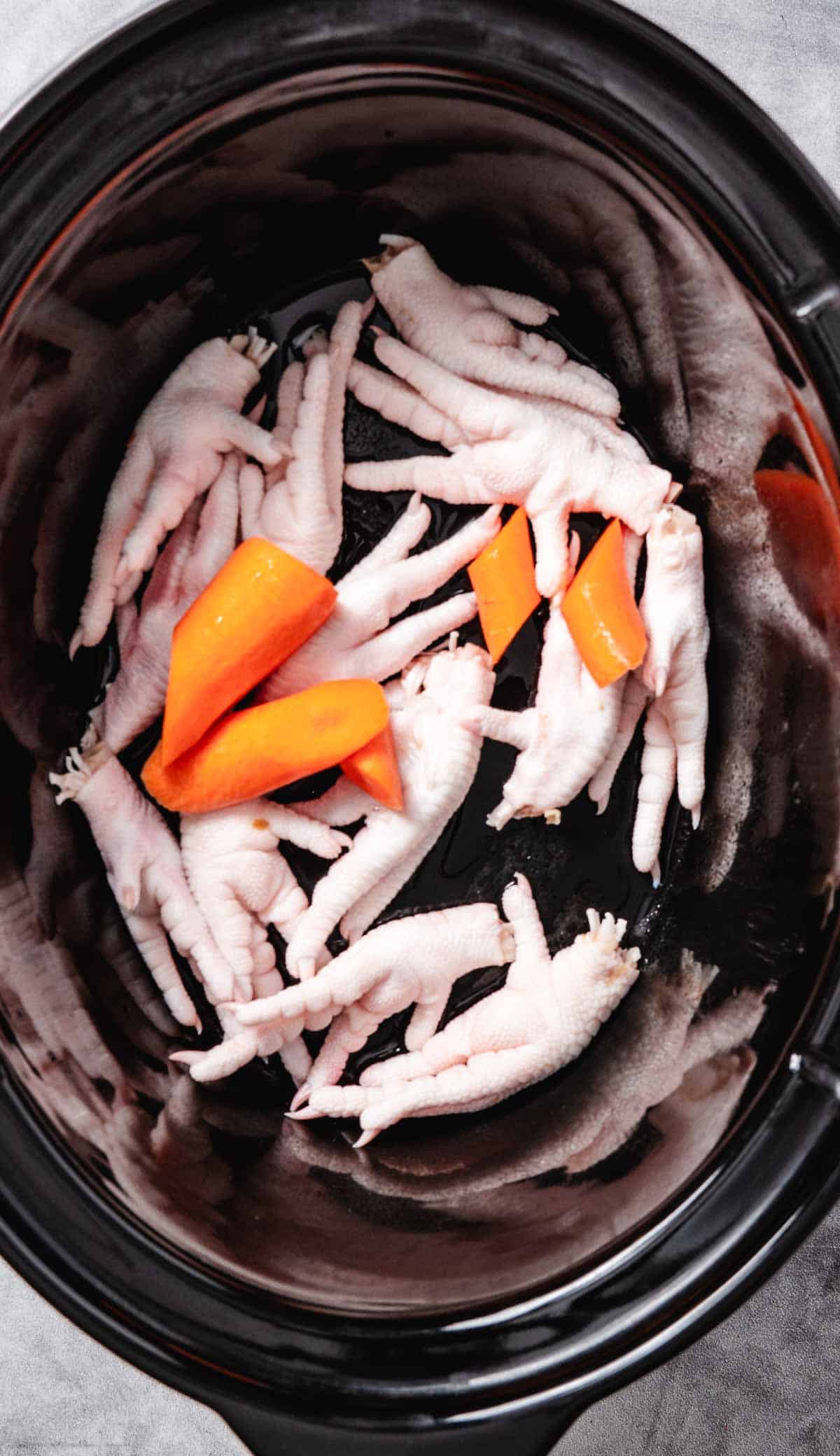 Chicken feet and carrots in a slow cooker.