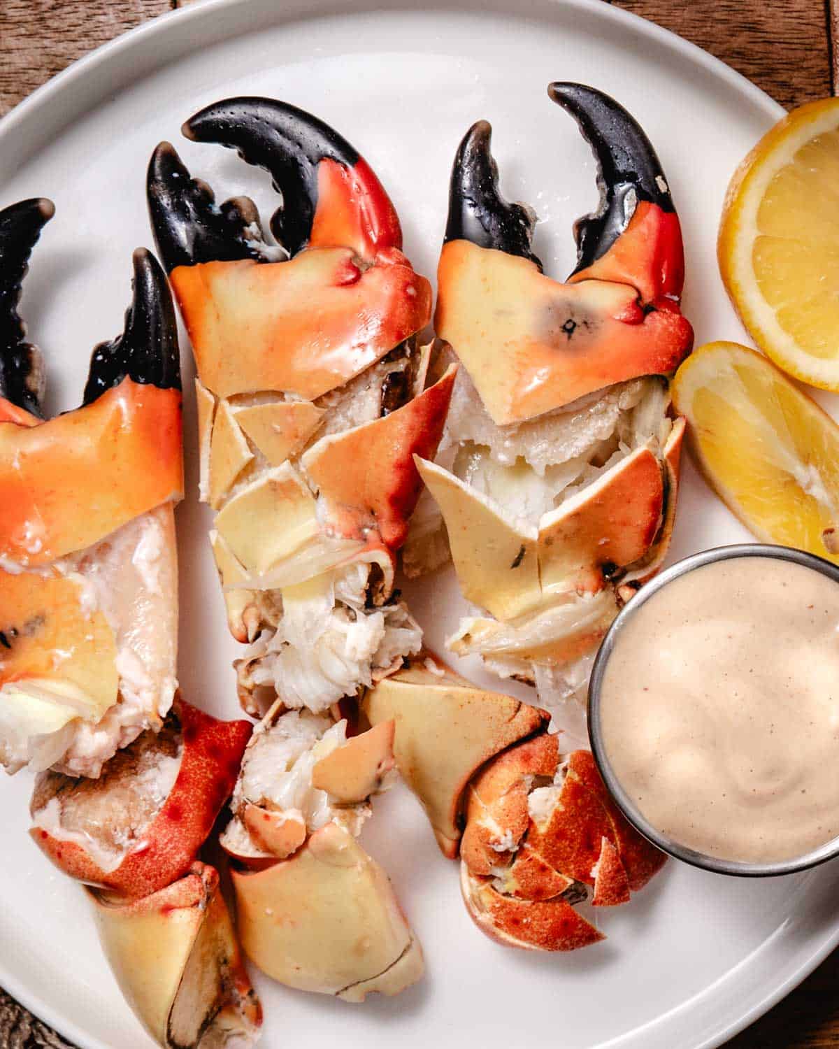 Stone crab claws served with creamy mustard sauce and fresh lemon wedges on a white plate. Fresh Florida stone crab claws are pre-cracked for easy serving.