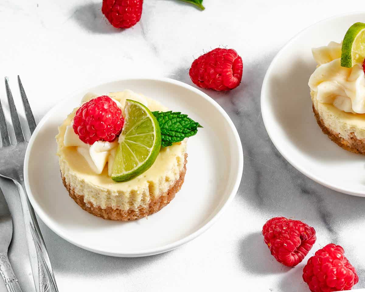 Key lime cheesecakes on white plates with raspberries and key limes.