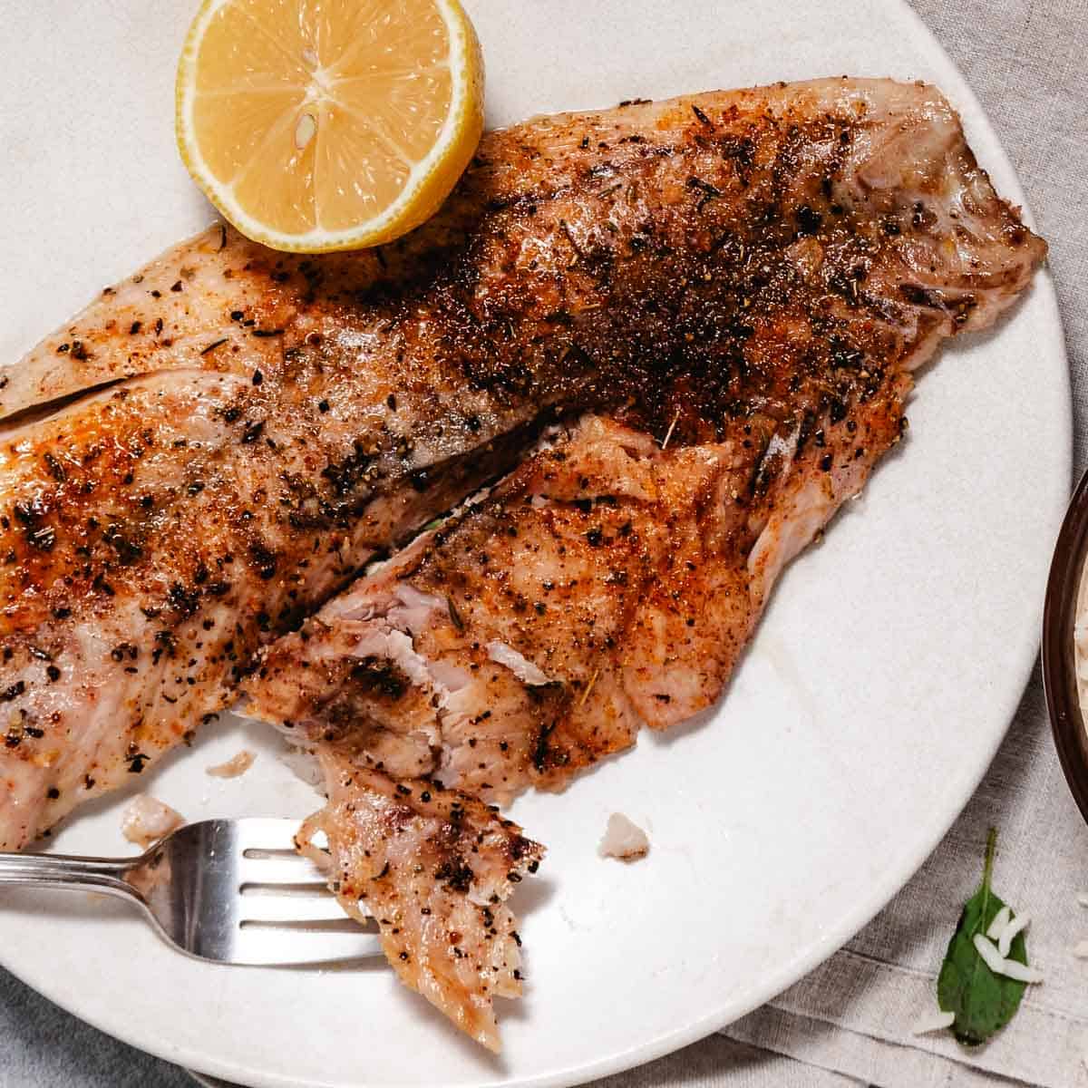 Broiled white fish with a half lemon on a white plate.