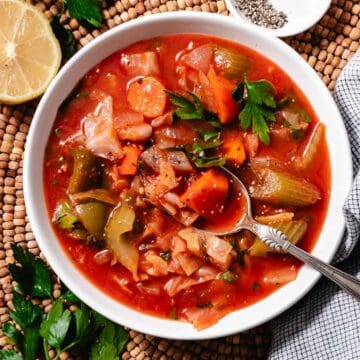 Cabbage and tomato soup in white bowl with lemon.