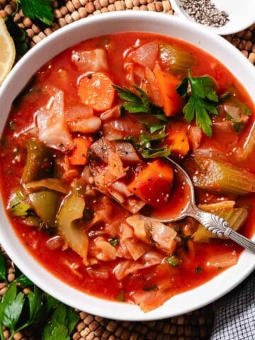 Cabbage and tomato soup in white bowl with lemon.