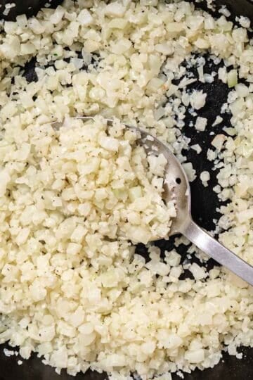 Fresh cauliflower rice cooking in butter and kosher salt in a skillet.