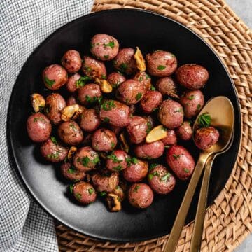 Roasted red potatoes in a bowl with gold spoons.