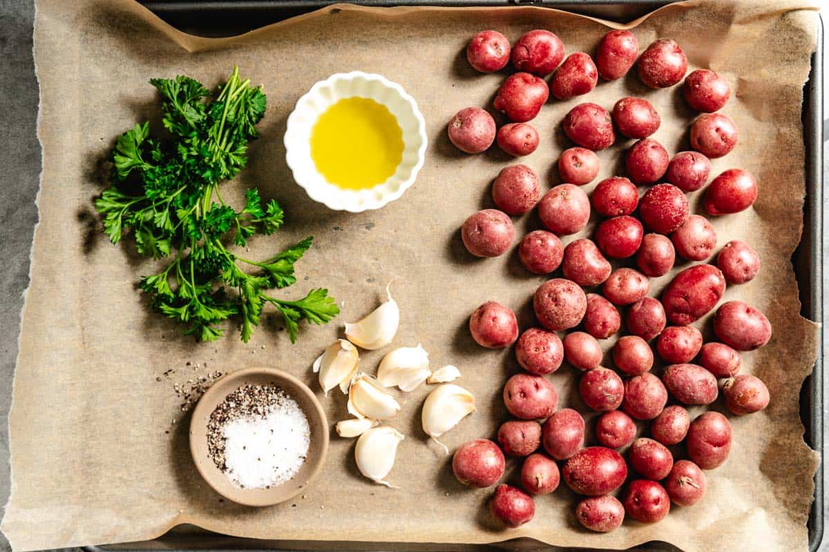 Potatoes, garlic, oil, salt, pepper, parsley on a sheet pan.